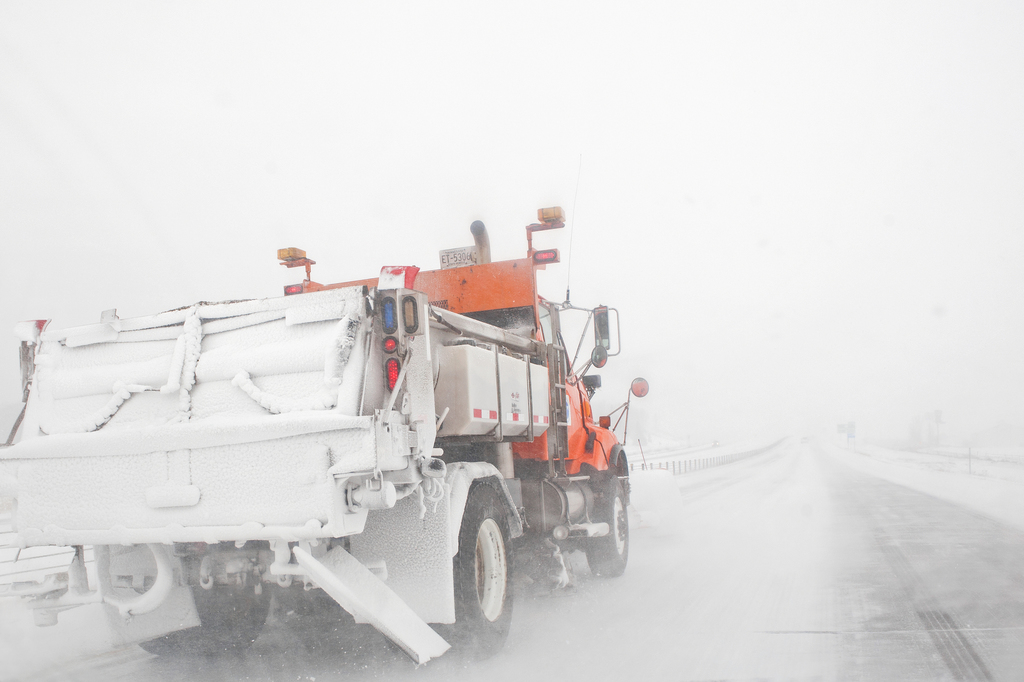Snow covered snow plow works to clear snow from rural highway